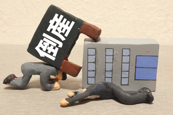 倒産と書かれた看板と倒れるビル・人の人形