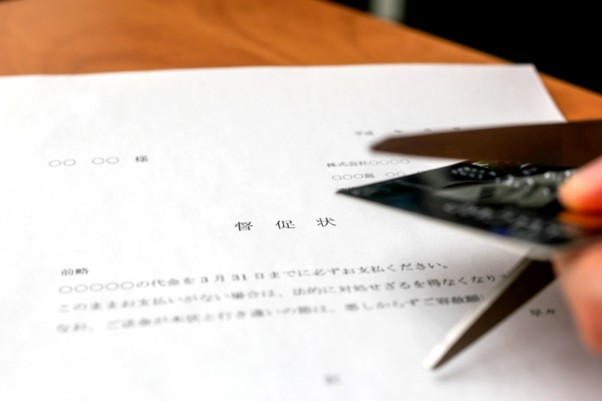 督促状とカードをはさみで切る手