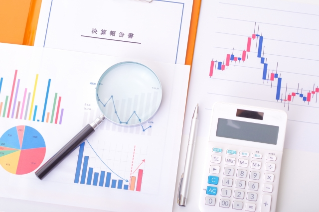 電卓と決算報告書と株価チャートと虫メガネ