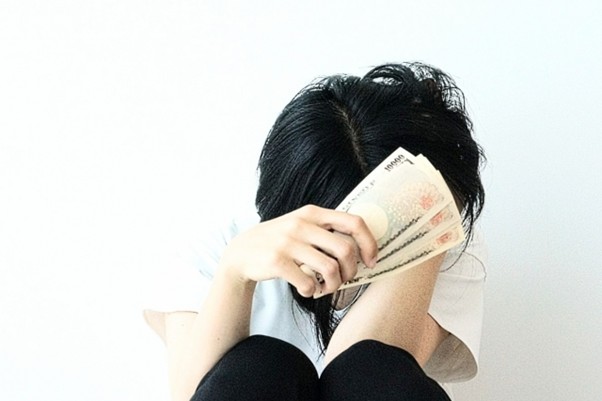 お金を握りしめて落ち込む女性